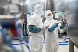 Medewerkers gekleed in witte disposable beschermkleding en PBM voeren hygiënecontroles uit.