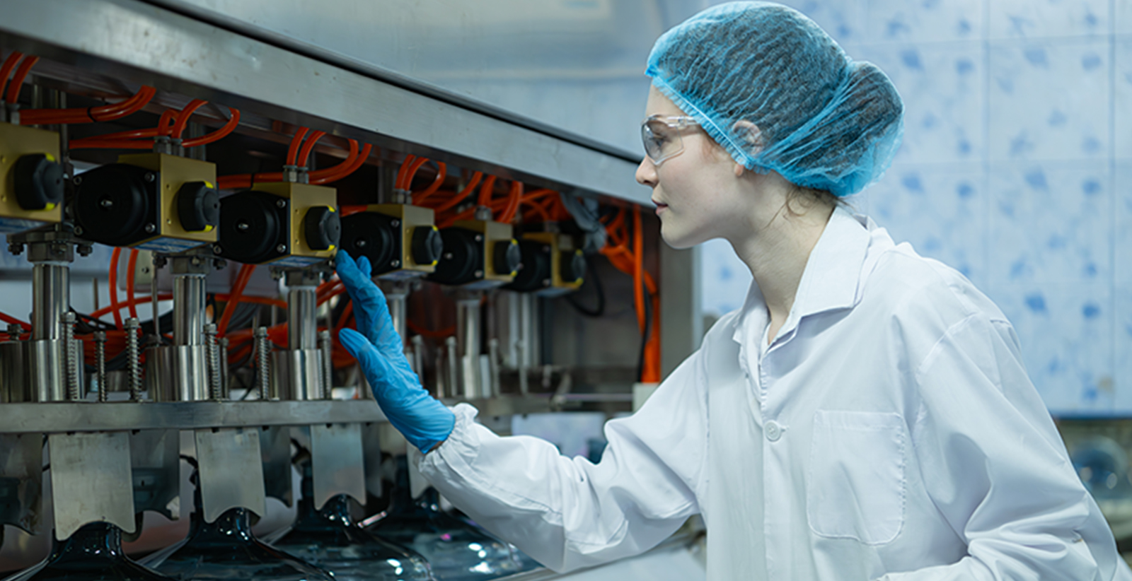 Een vrouwelijke medewerker gekleed in witte hygiënische beschermkleding en PBM voert hygiënecontroles uit.