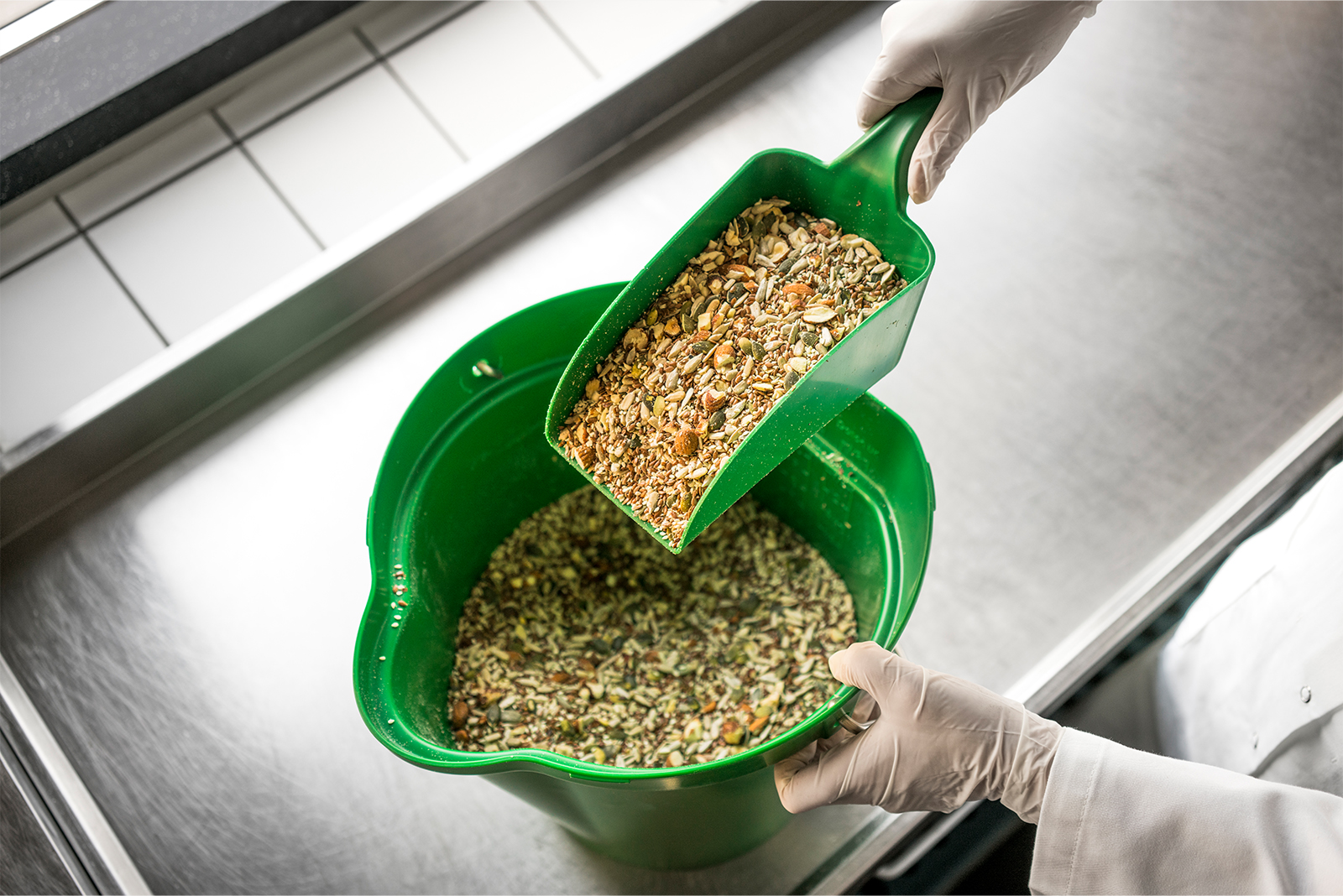 Toevoegen van zadenmix aan groene kunststof emmer in een productieruimte