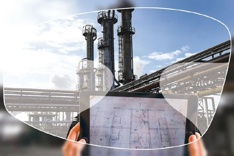 Industriële installatie met pijpleidingen en torens, bekeken door een veiligheidsbril terwijl iemand een technische tekening op een tablet vasthoudt.