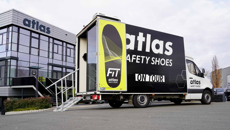 Atlas Safety Shoes-demovoertuig geparkeerd voor een bedrijfsgebouw, voorzien van FIT ON TOUR-branding.