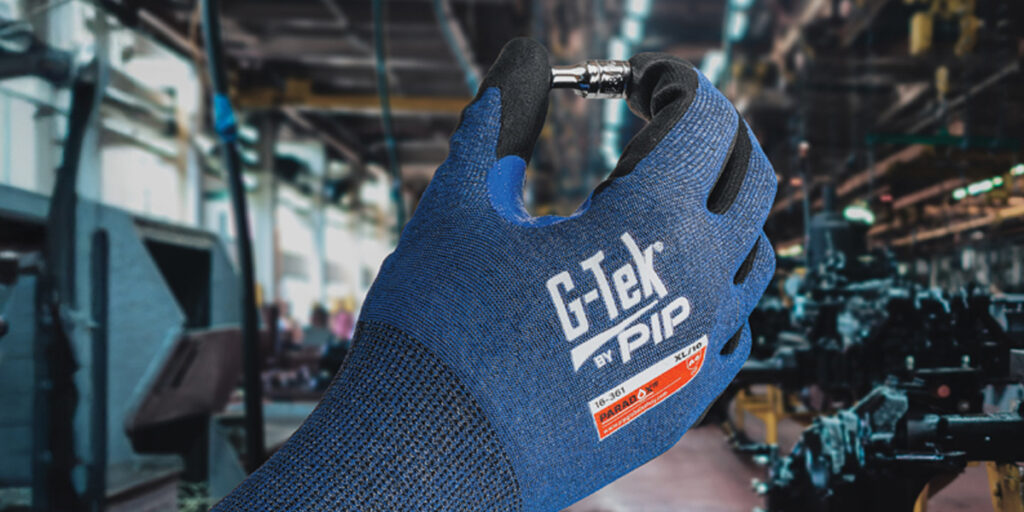 Hand met een blauwe snijbestendige werkhandschoen houdt een metalen bout vast in een industriële omgeving.