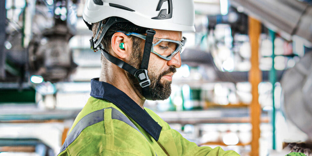 Medewerker in een industriële omgeving draagt veiligheidshelm, veiligheidsbril en gehoorbescherming tijdens werkzaamheden.