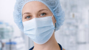 An image of a female doctor in a medical environment wearing a hairnet and face mask.