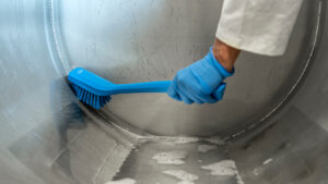 A stainless-steel round object is being cleaned with a blue Vikan brush.