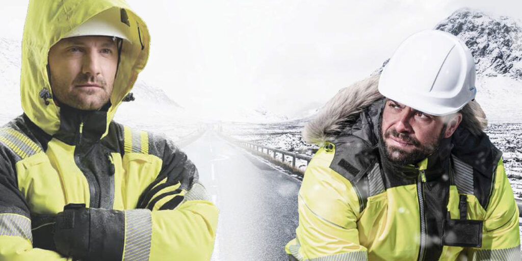 Two workers wearing Hi-Vis winter workwear and safety helmets in a cold, snowy environment.