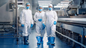 Employees wearing white disposable protective clothing walk through a food production area.