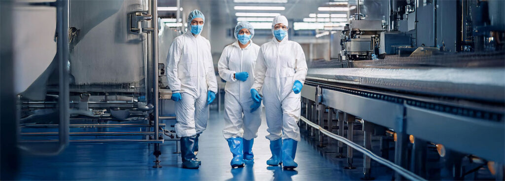 Employees wearing white disposable protective clothing walk through a food production area.