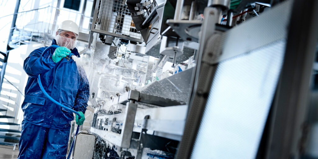 An employee cleaning an industrial machine with a water jet