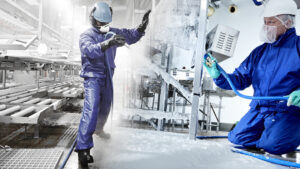 Two workers wearing blue protective clothing clean machinery and floors in an industrial production environment.