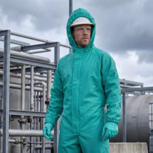 Worker wearing green ELKA PVC protective clothing with a hood, gloves, safety goggles and a helmet in an industrial environment.